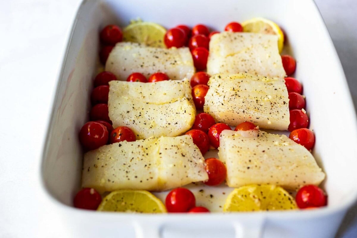 cod placed in a baking dish with tomatoes and lemons.