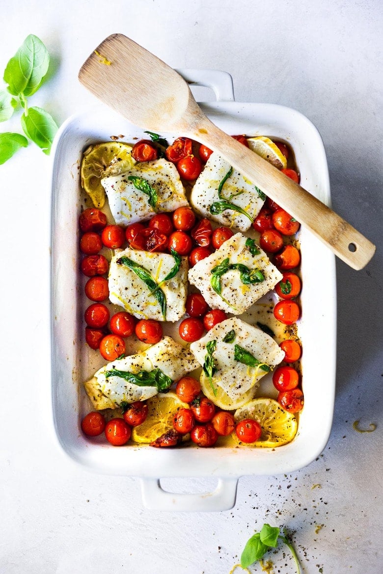 baking dish with baked cod with burst tomatoes topped with wilted basil and lemon zest. 
