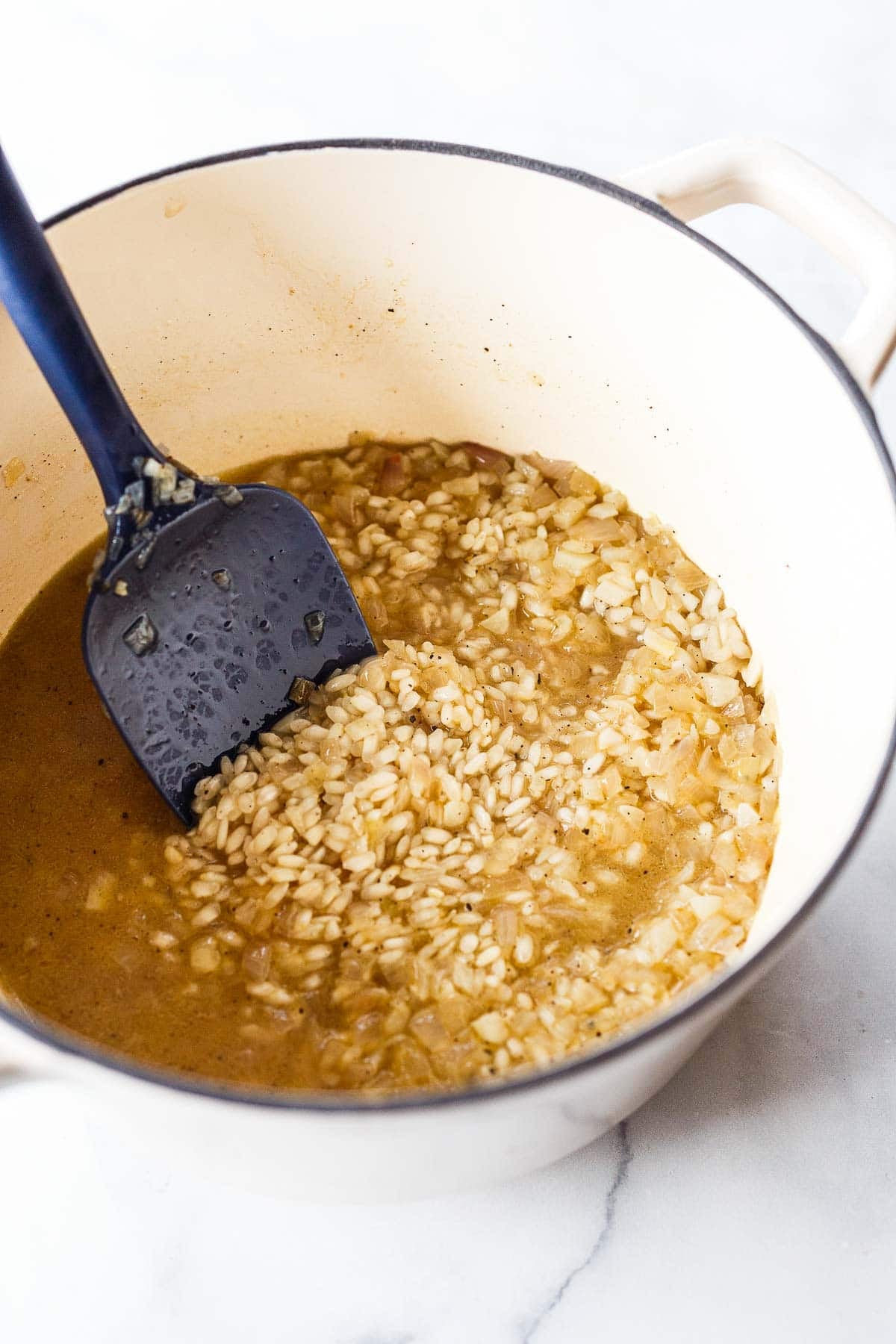dutch oven with arborio rice, broth, and aromatics, with silicone spatula to stir.