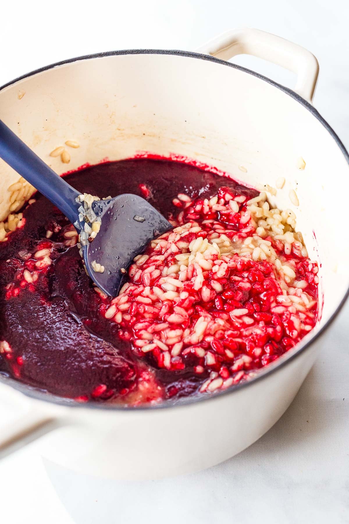 dutch oven with beet purée mixed into risotto with silicone spatula. 