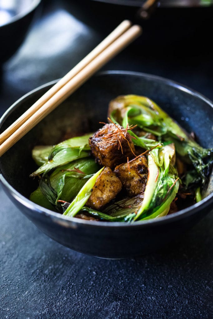 bowl of bok choy topped with black pepper tofu with chopsticks on top of the bowl. 
