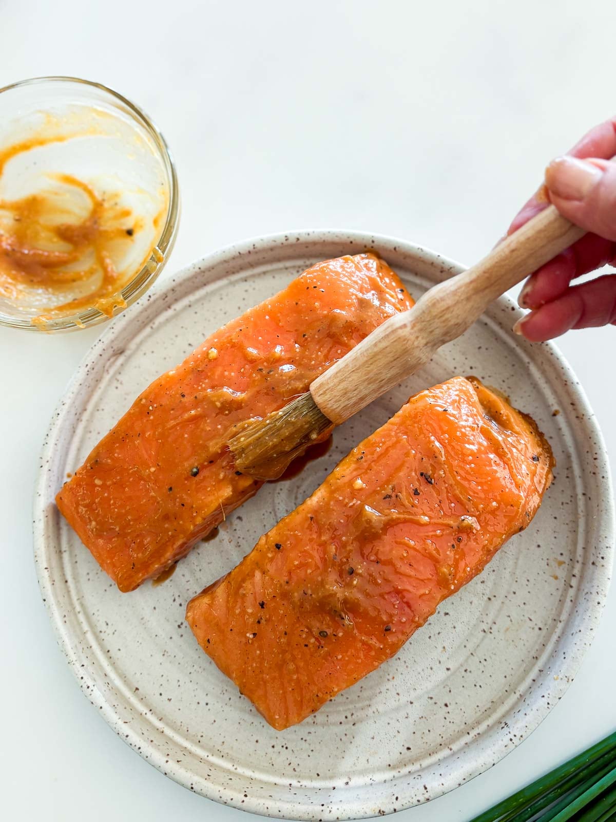 hand using wooden brush to brush marinade onto the two salmon filets on a plate. 