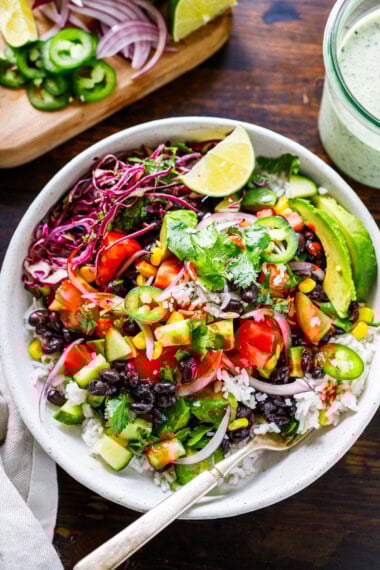 Our favorite burrito bowl recipe is made with seasoned black beans and rice topped with fresh tomatoes, avocado, corn, shredded cabbage, and a vegan cilantro lime crema.