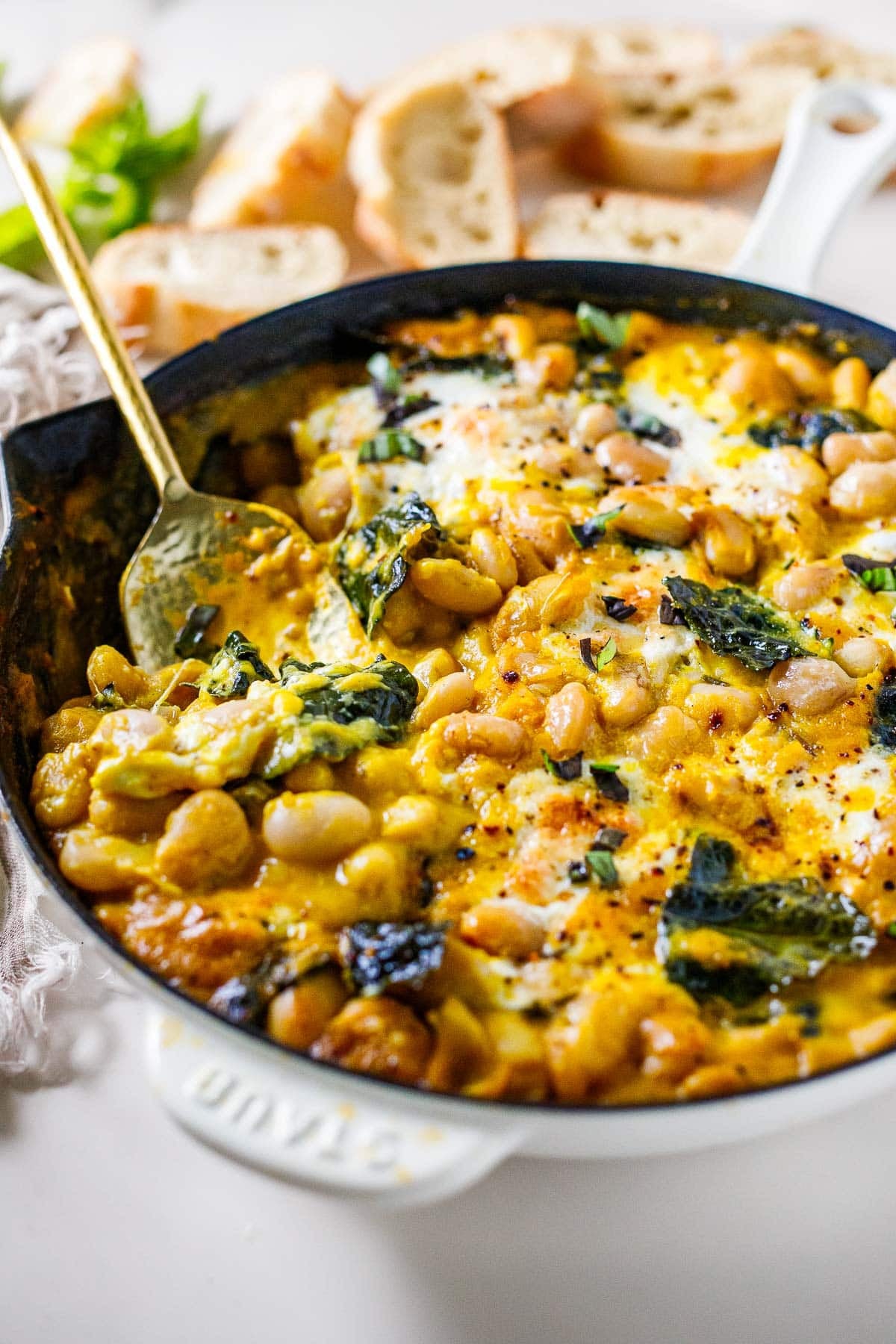 skillet with butternut baked beans with burrata, kale, and chili flakes, with spoon.