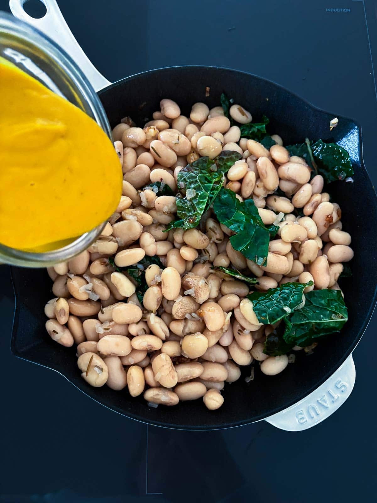 pouring butternut sauce into skillet with white beans and kale.