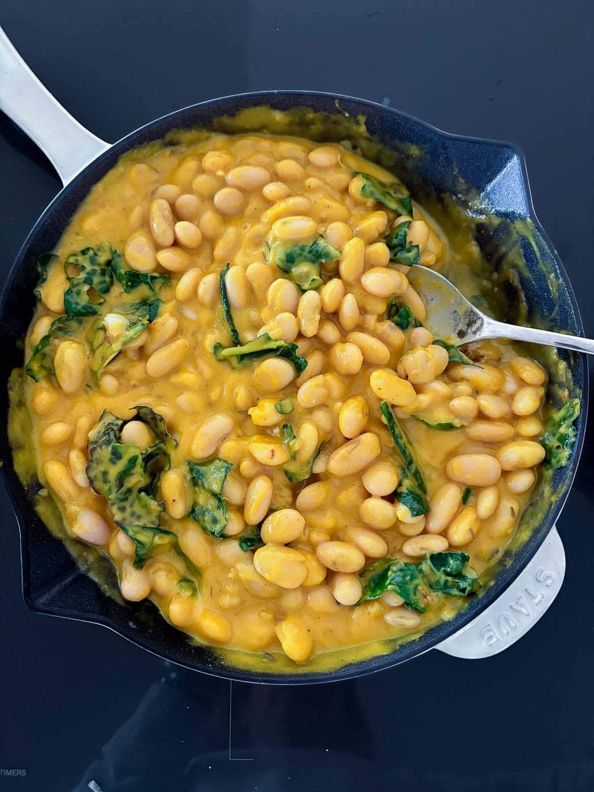 skillet with butternut squash sauce, white beans, and kale mixed together with spoon.
