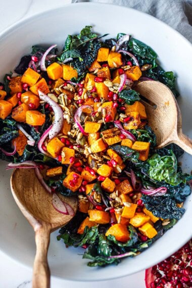 bowl of butternut squash kale salad topped with red onion, seeds, pomegranate seeds, and dried cranberries.