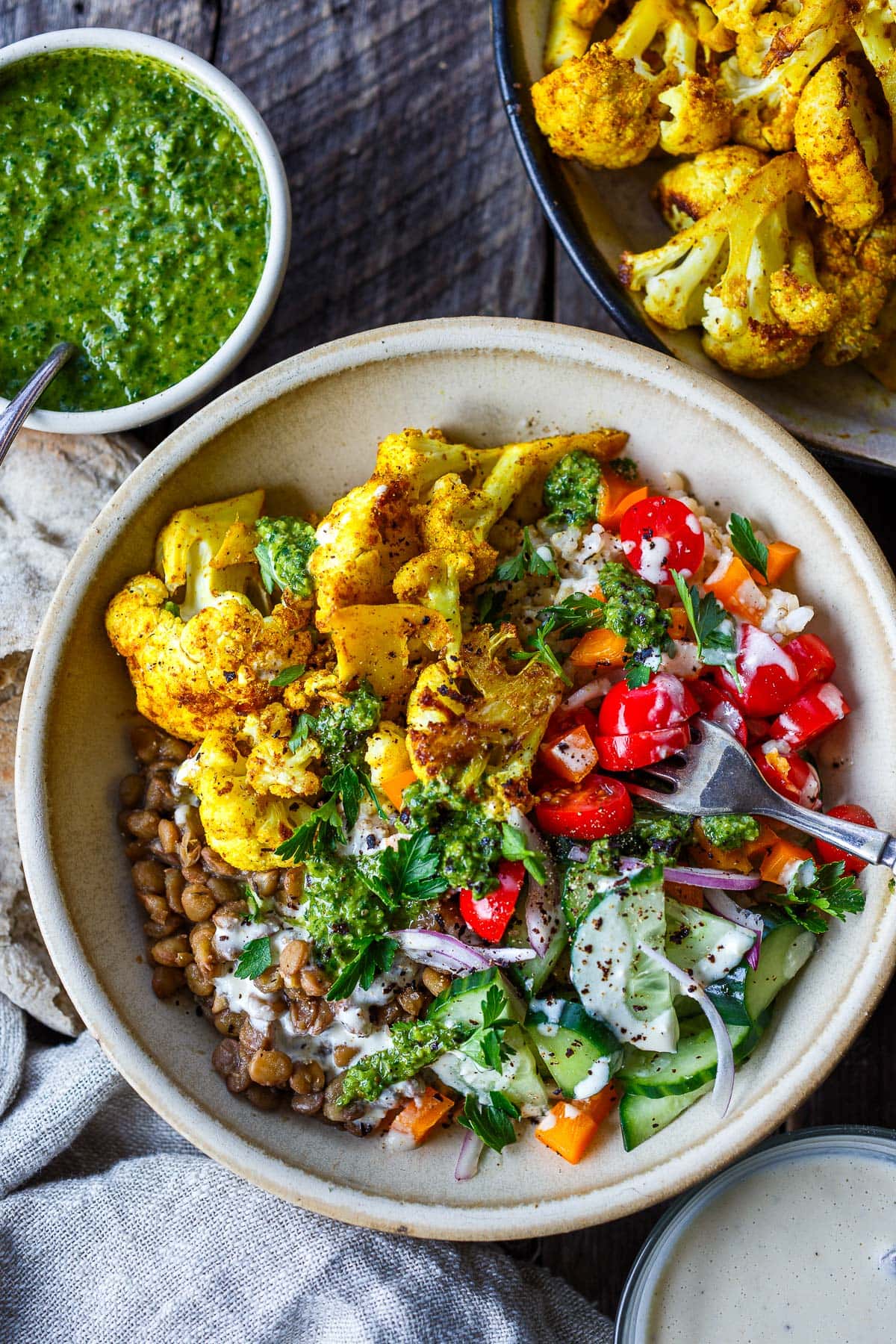 bowl of cauliflower shawarma with lentils, tomatoes, cucumber, onion, zhoug and tahini sauce.
