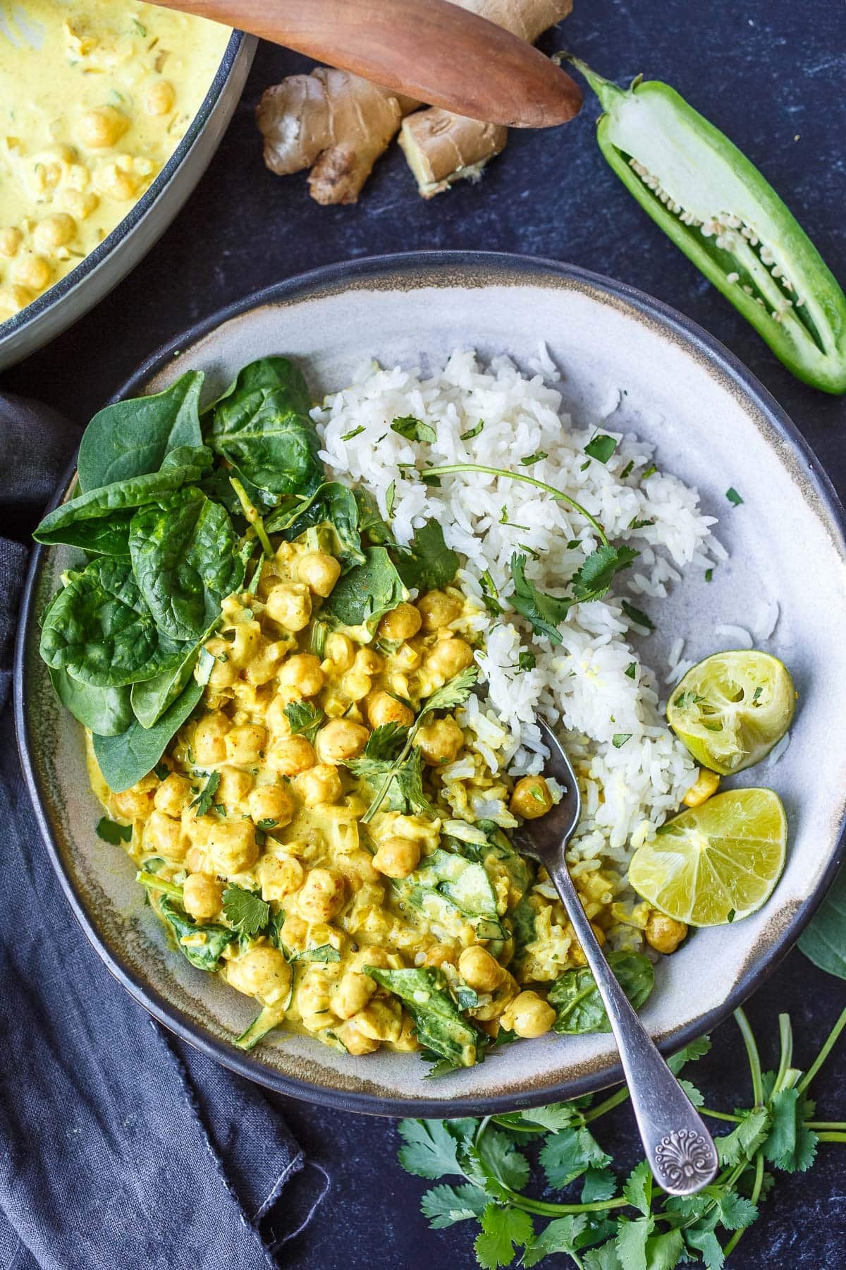 bowl of golden chickpea curry over basmati rice with fresh spinach, cilantro, and lime wedges.