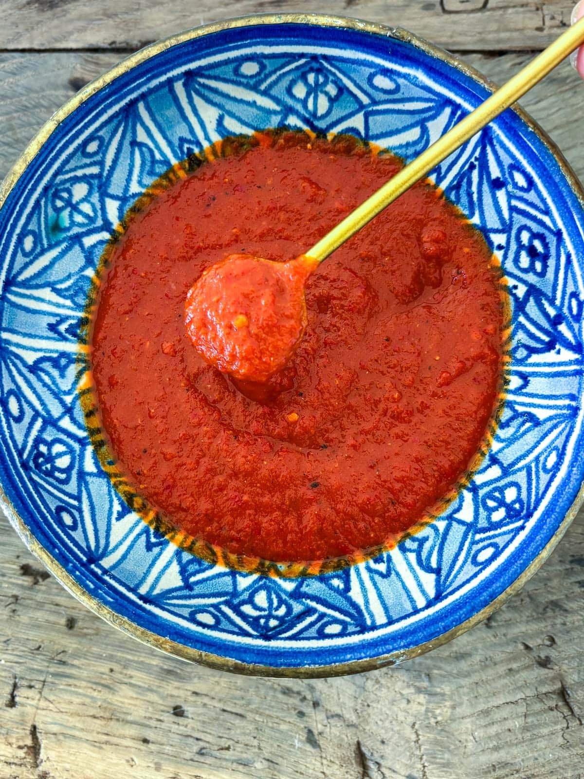 gold spoon lifting up chili garlic sauce from blue bowl. 