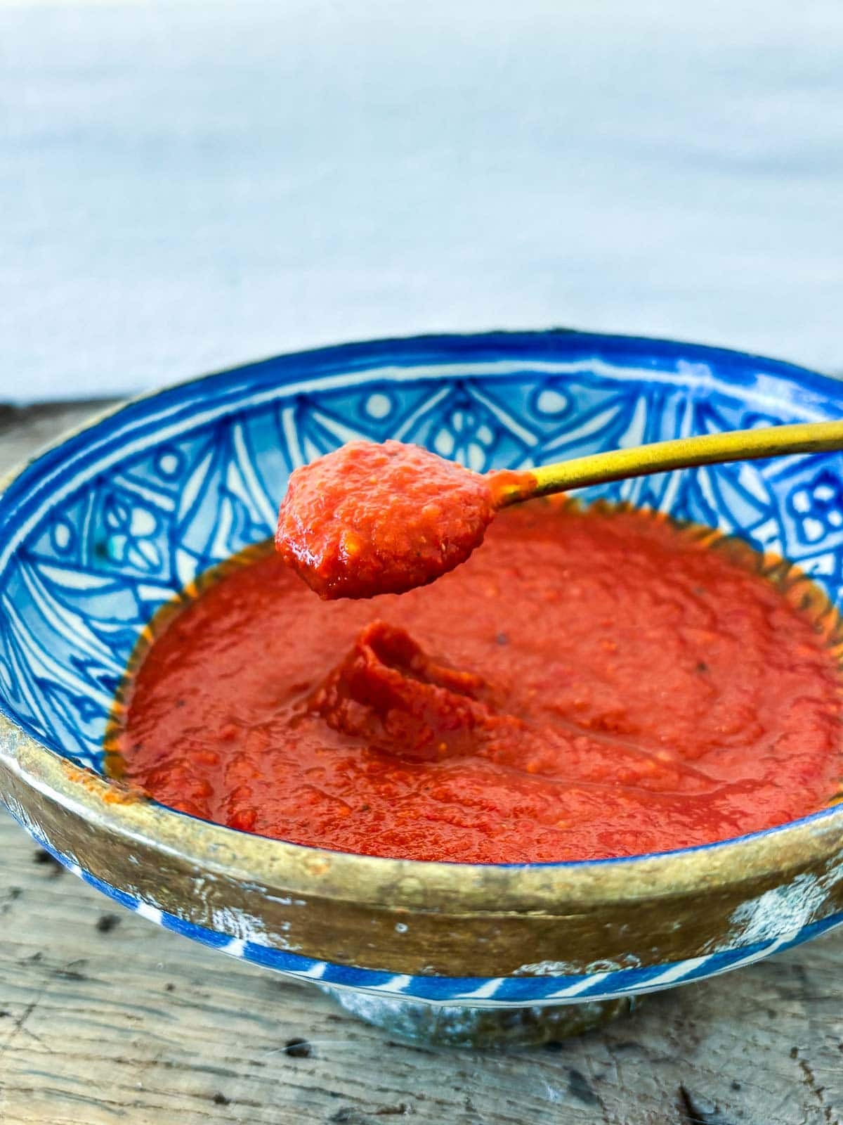 gold spoon lifting up a spoonful of chili garlic sauce from blue bowl.