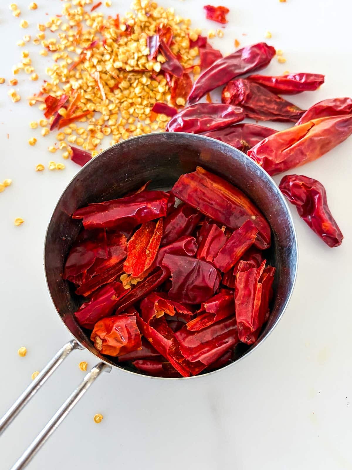 measuring cup with packed and de-seeded red chilies with seeds left to the side. 