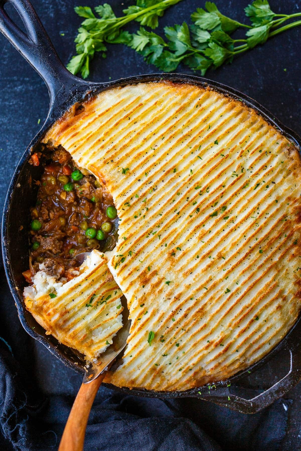 cast iron skillet with cottage pie with broiled mashed potato topping and a scoop removed revealing meaty veggie filling.