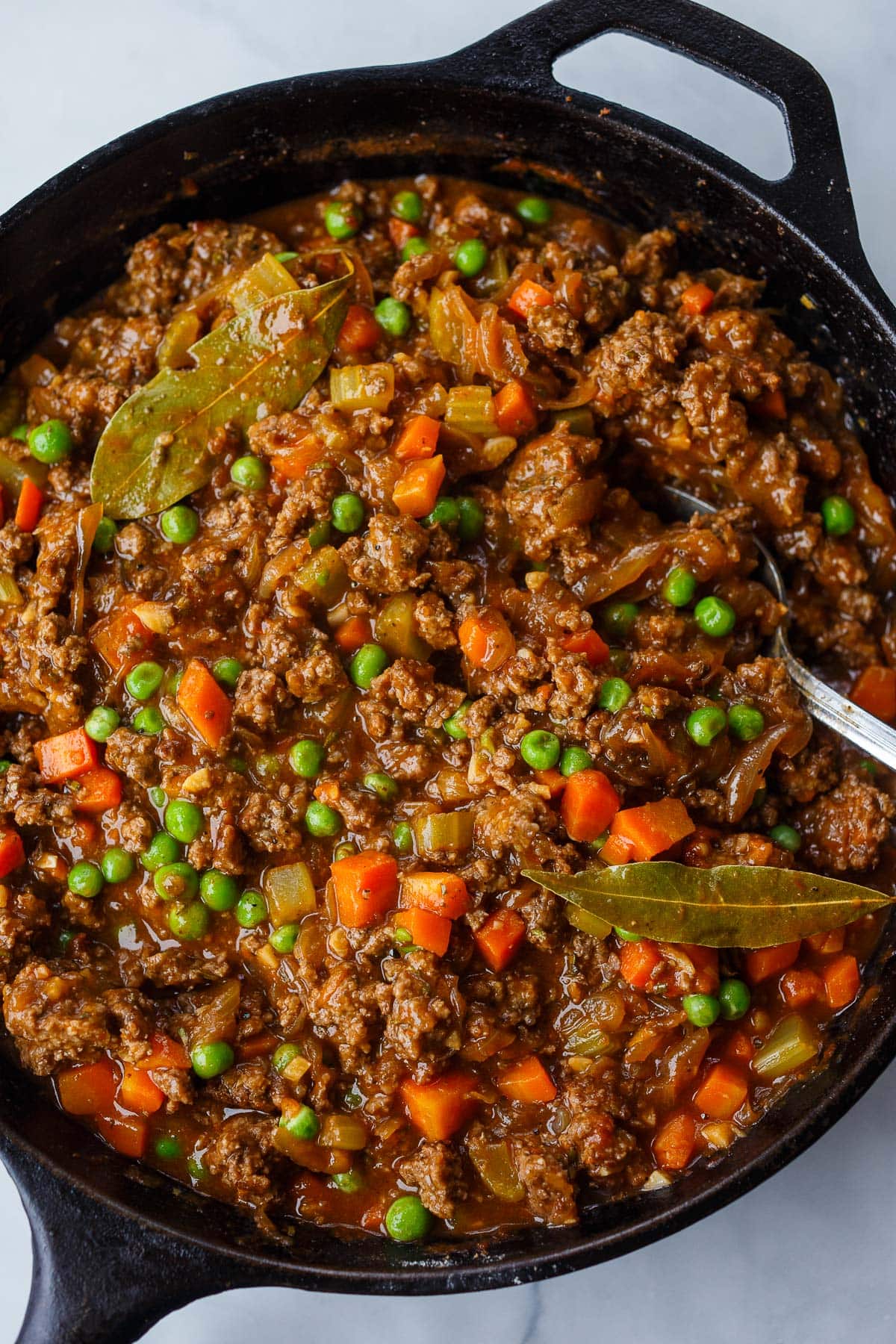 cast iron skillet with cottage pie filling with bay leaves.