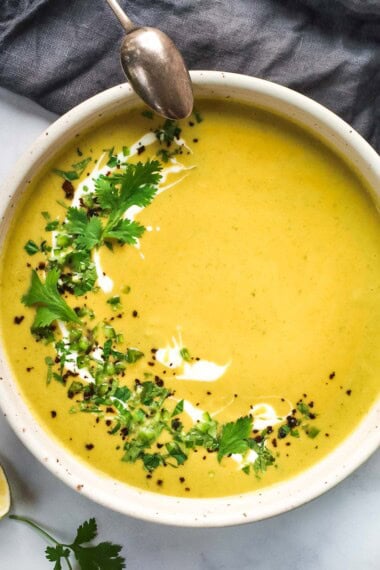bowl of curried zucchini soup garnished with yogurt and fresh mint and cilantro.