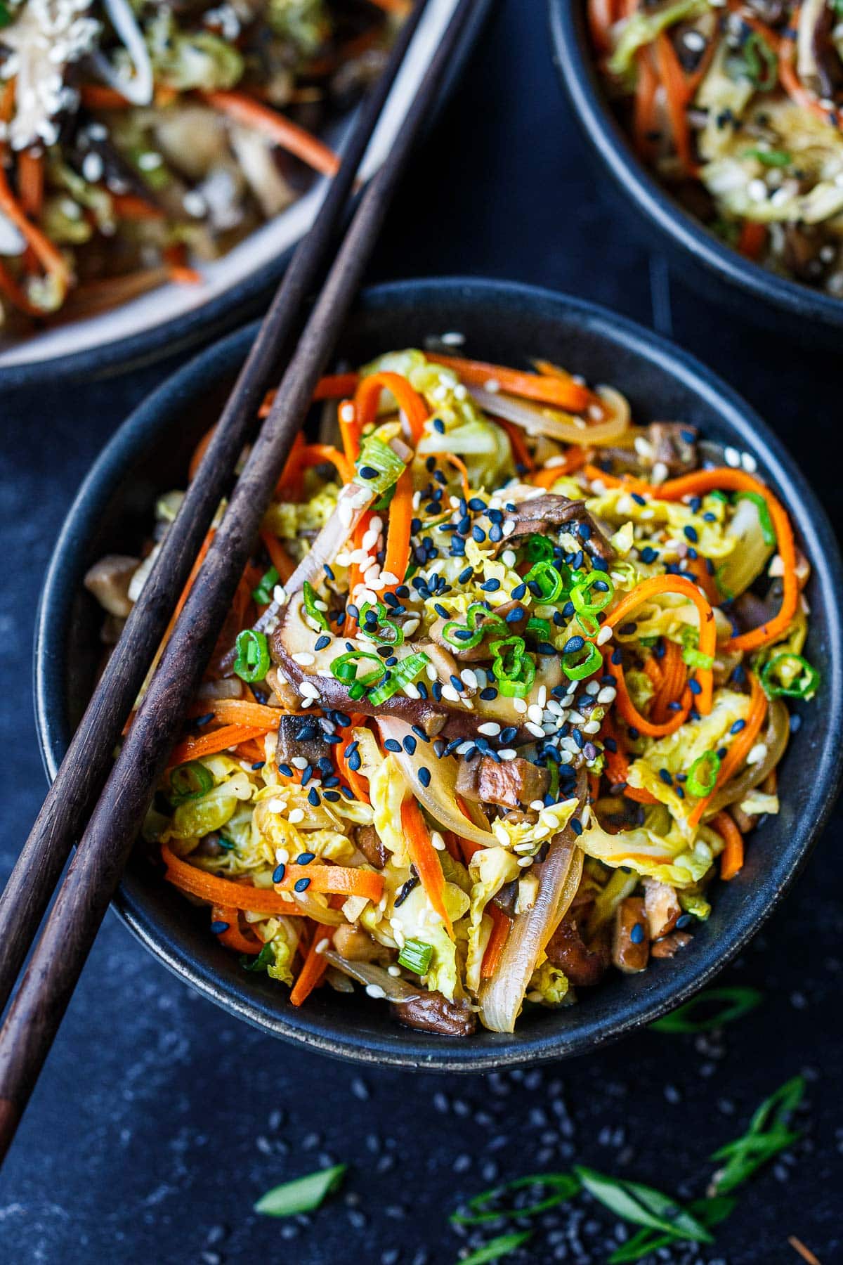 deconstructed egg roll in a bowl with carrots, cabbage, onions, and mushrooms garnished with green onions and sesame seeds topped with wood chopsticks. 