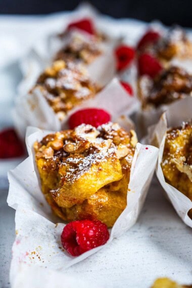 French toast muffins in paper liners, topped with nuts, powdered sugar, and raspberries.
