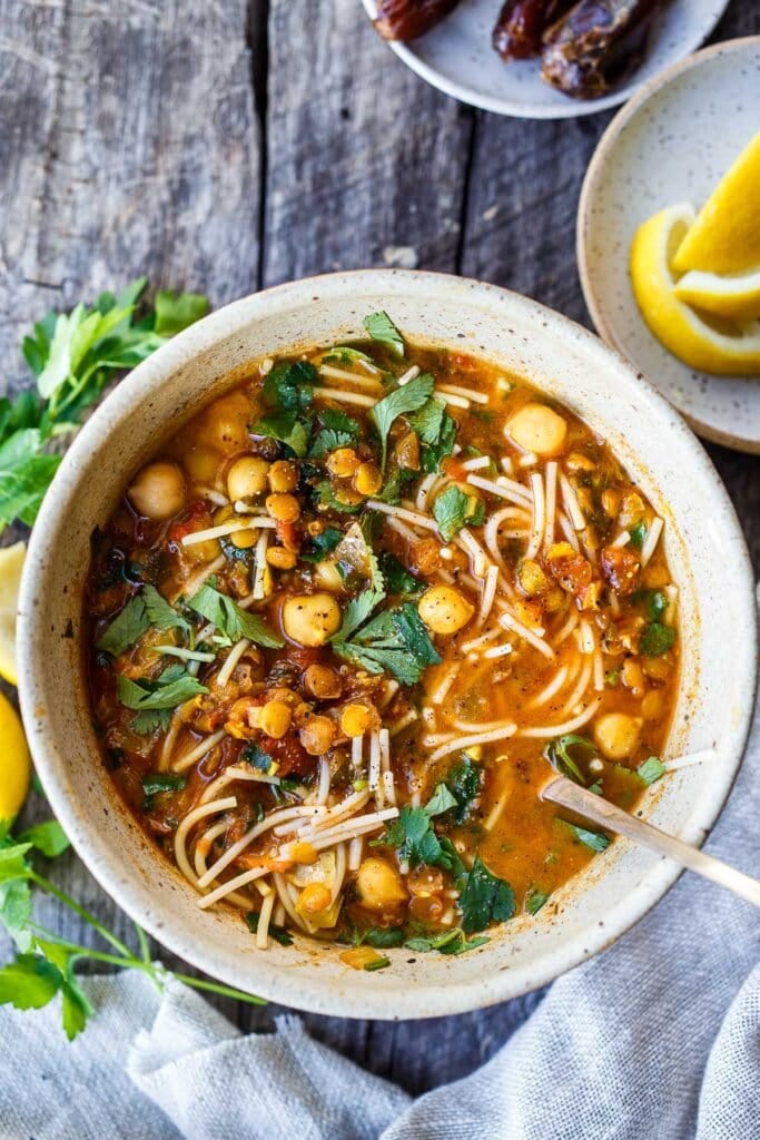 harira soup with noodles, chickpeas, and lentils in a bowl with fresh herbs. 