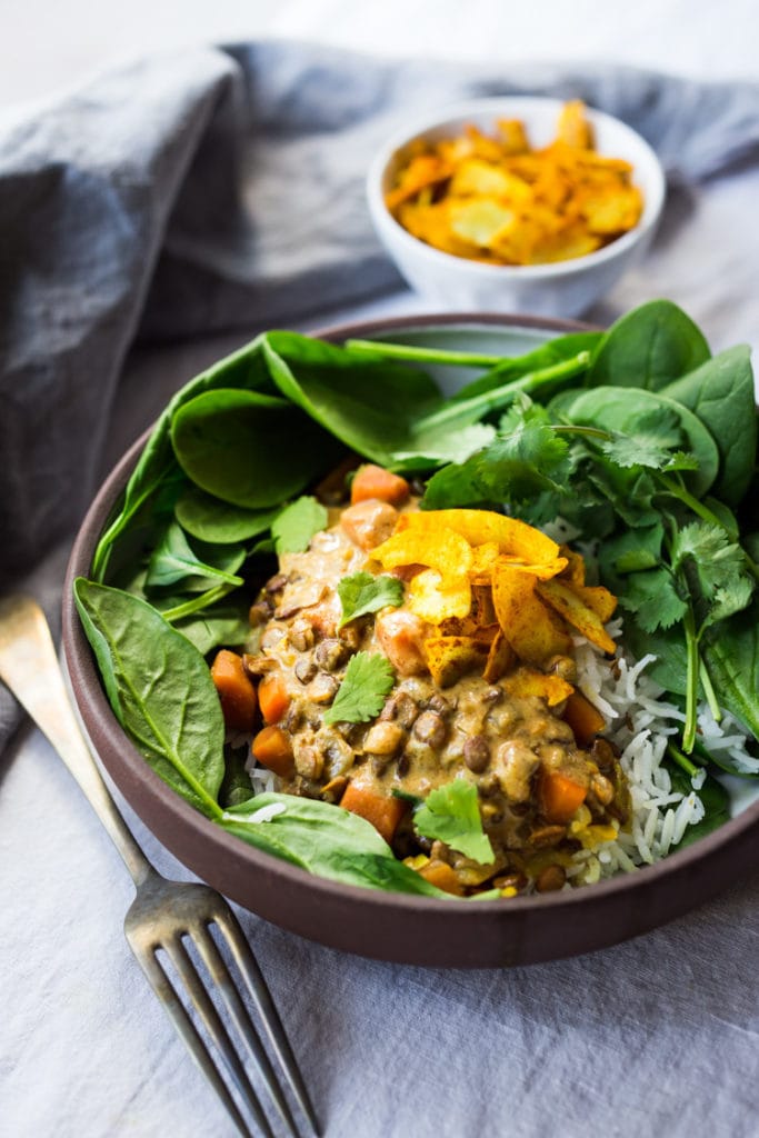 bowl of lentil curry over basmati rice and fresh spinach, topped with toasted coconut and cilantro.