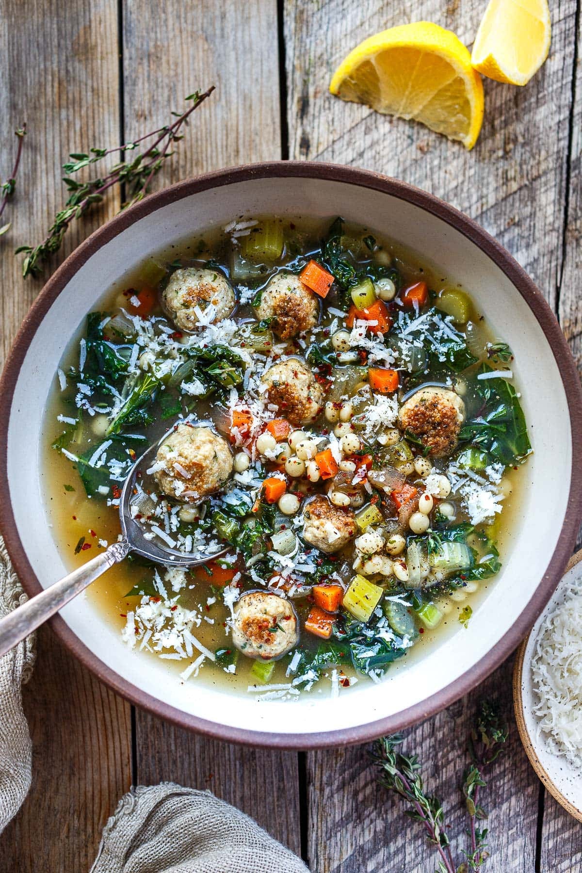bowl of Italian wedding soup with meatballs, pearl couscous, veggies, kale, and parmesan with spoon. 