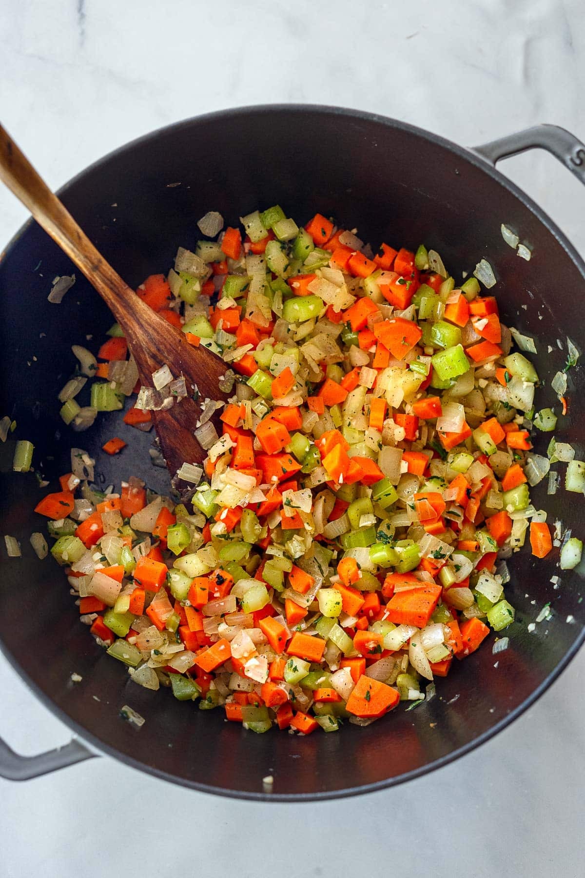 wood spoon stirring sautéed onion, carrot, and celery in Dutch oven. 