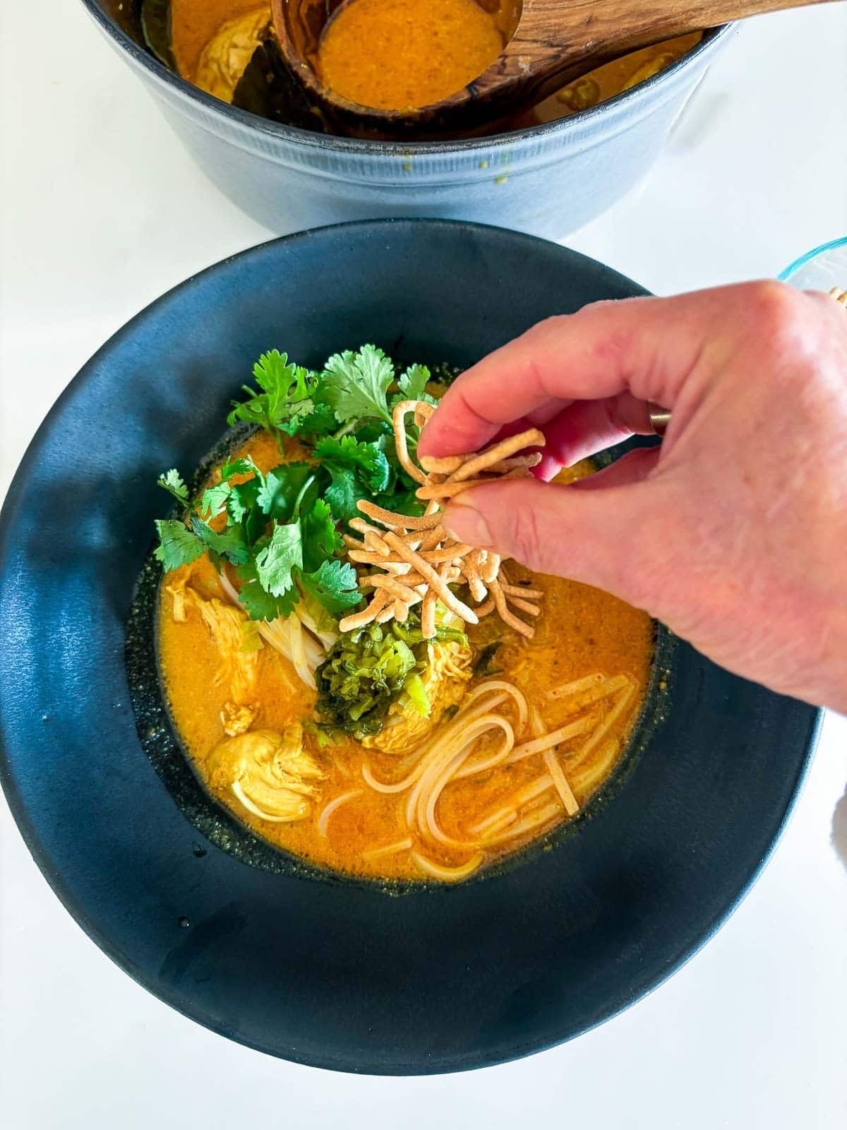 Garnishing the soup with mustard greens, crunchy noodles and cilantro and lime. 