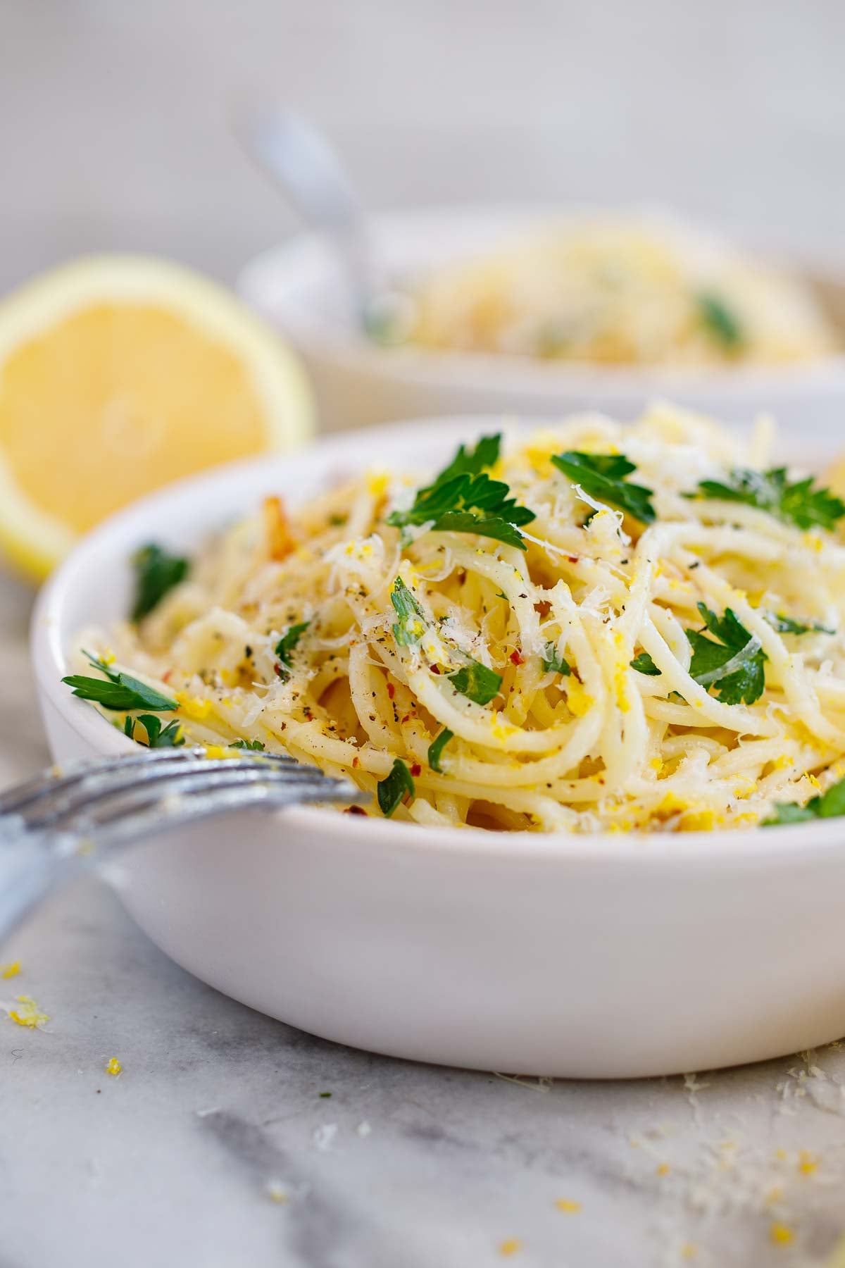 pasta bowl side view with lemon pasta with red pepper flakes, pecorino, and parsley with a fork resting upside down against the bowl. 