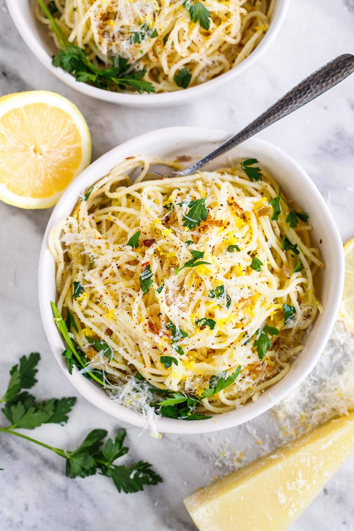 bowl of lemon pasta with pecorino, lemon zest, and parsley, beside lemon half, fresh parsley, and pecorino wedge. 