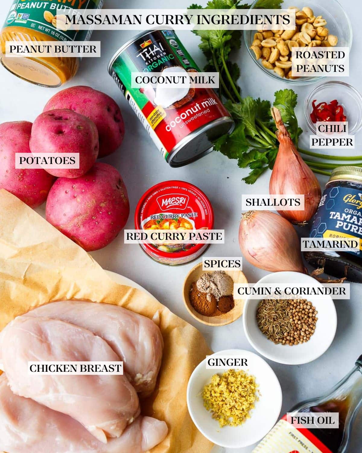 ingredients for thai massaman curry laid out - peanut butter, coconut milk, cilantro, peanuts, red chilies, red potatoes, red curry paste, shallots, tamarind puree, spices, seeds, ginger, fish sauce, chicken. 
