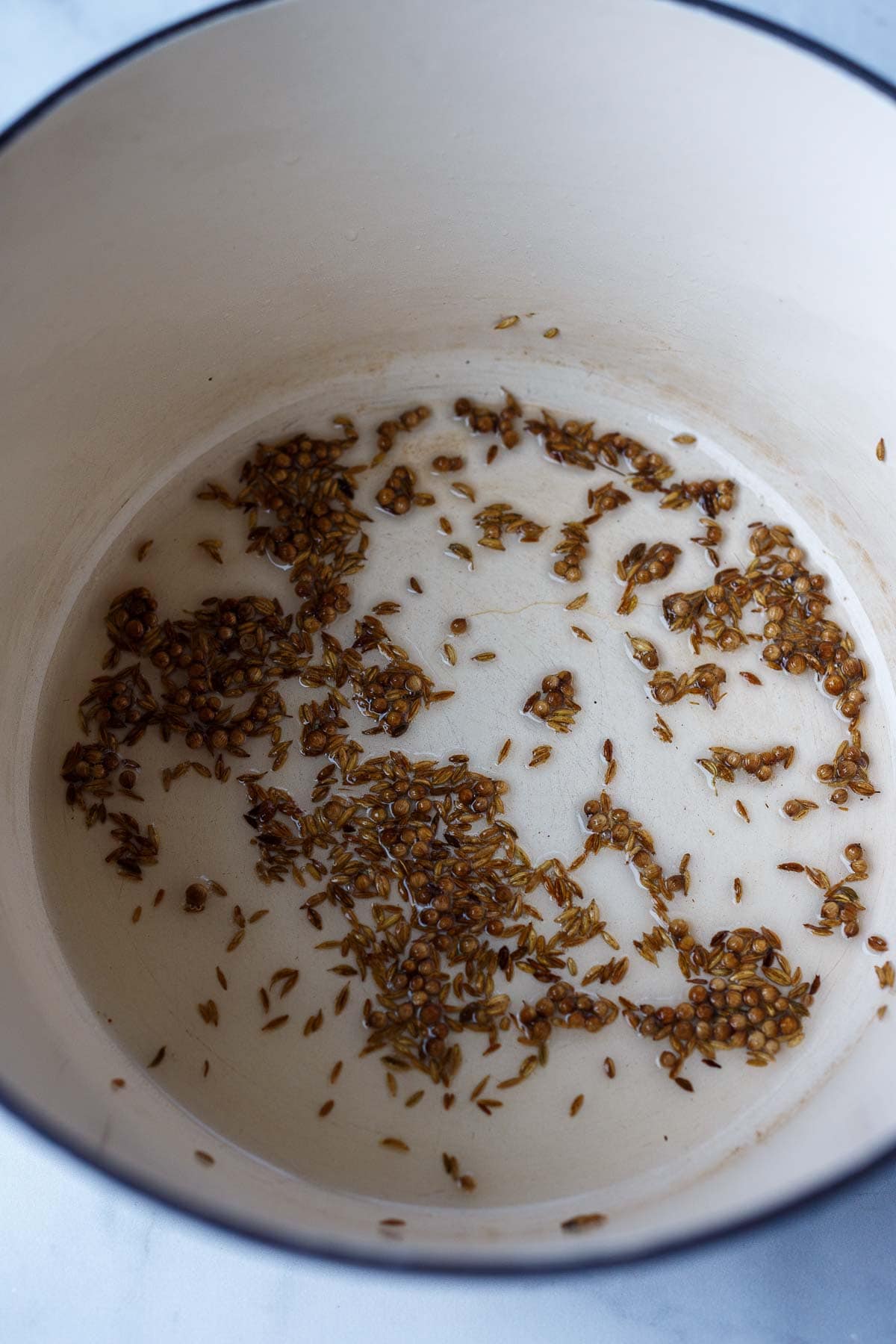 coriander seeds and cumin seeds in pot with coconut oil. 
