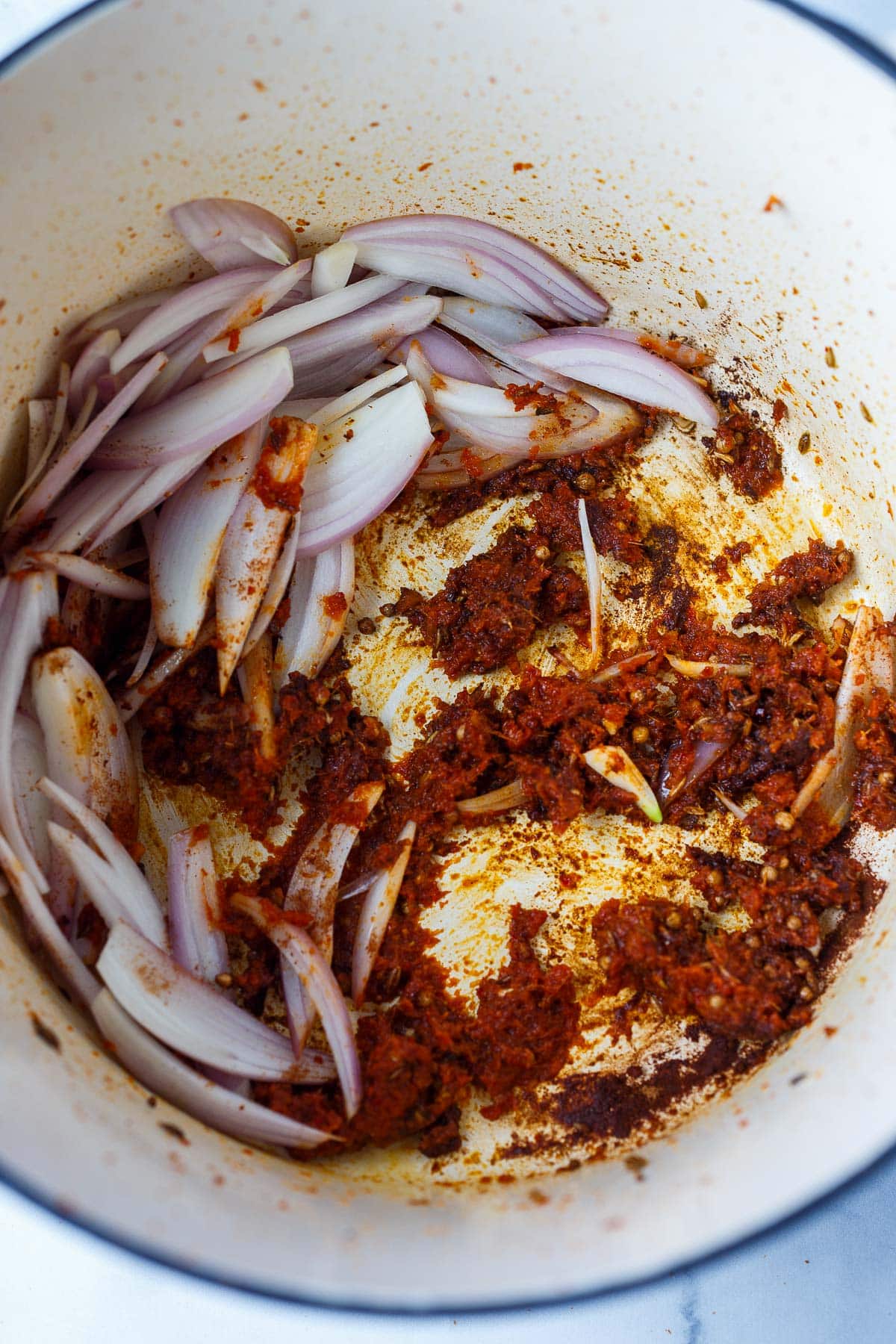 sliced shallots and red curry paste with seeds and spices sautéing in pot.