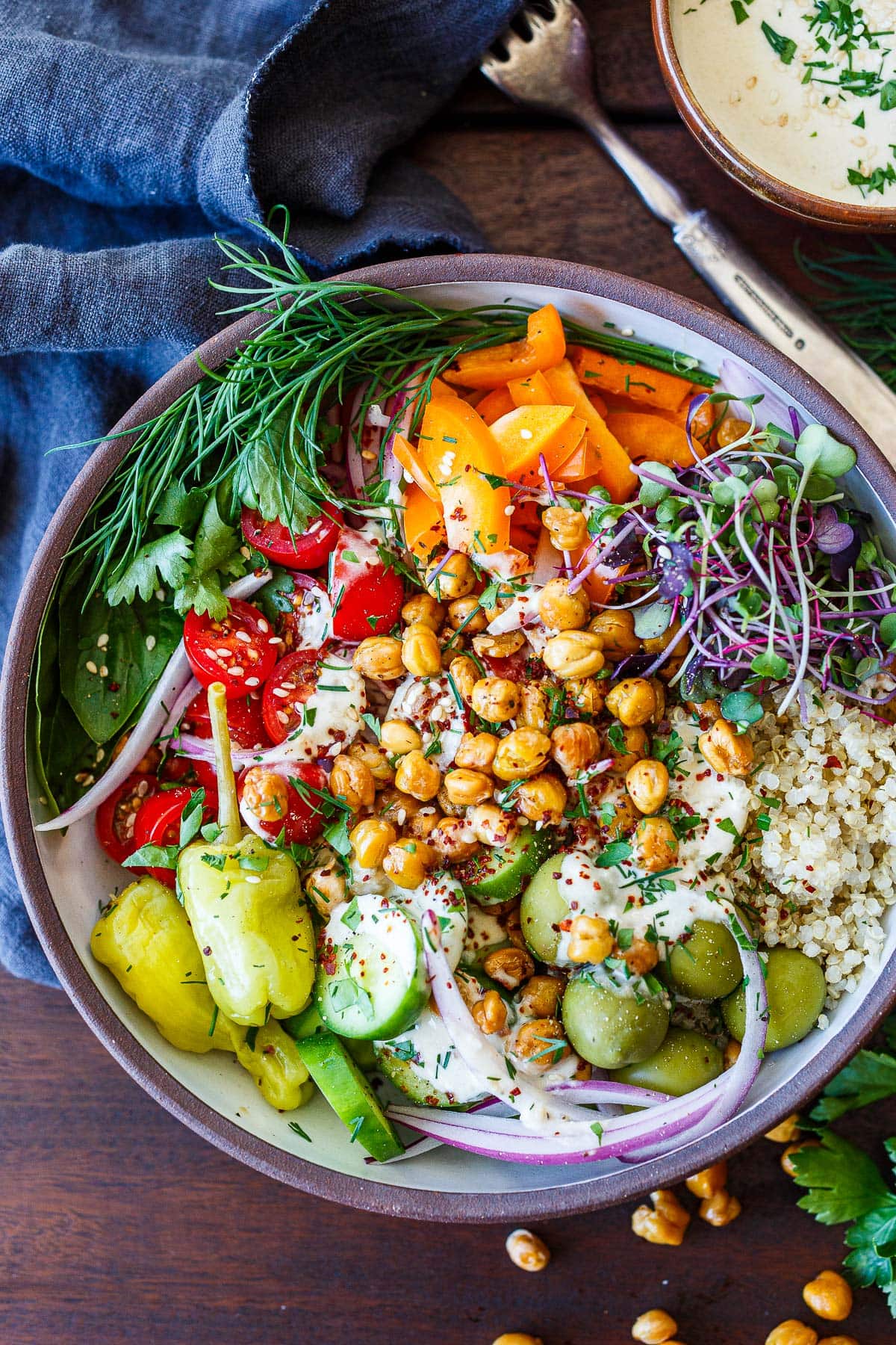 crispy Mediterranean chickpea bowls with orange bell pepper, microgreens, dill, parsley, basil, cherry tomatoes, red onion, peperoncini, cucumber, and green olives over quinoa with tahini sauce.