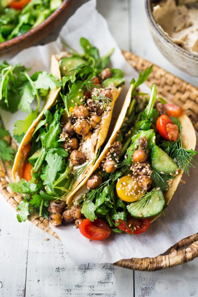 two Middle Eastern salad tacos topped with chickpeas, cucumber, cherry tomatoes, dill, parsley, arugula, and za'tar.