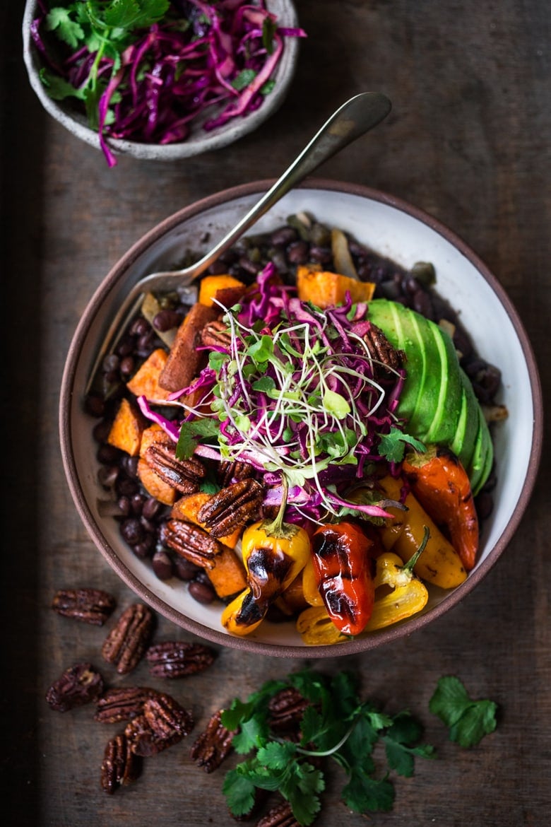 vegan Oaxacan bowl with black beans, onions, sweet potatoes, charred peppers, cabbage slaw, micro greens, and sliced avocado.