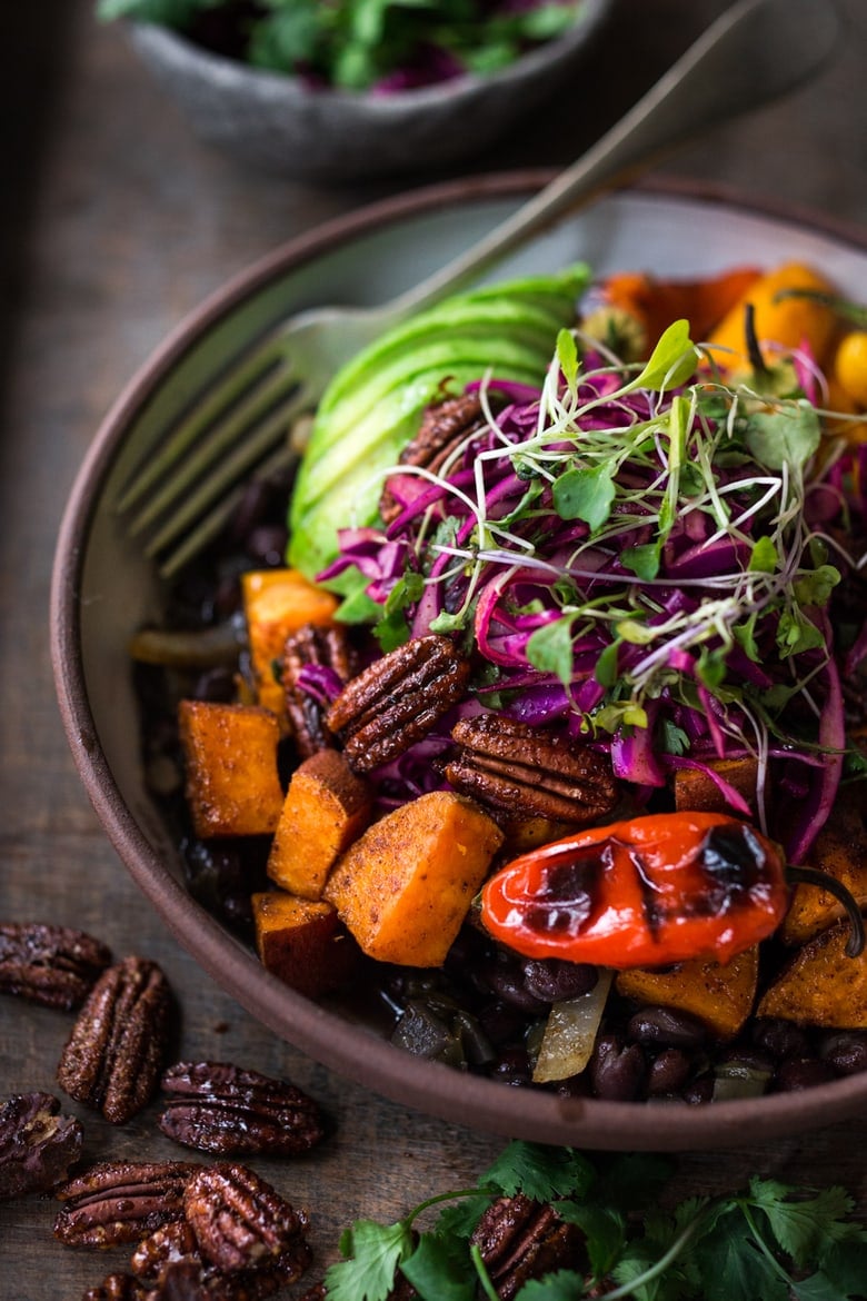 spicy Mexican Oaxacan bowl with base of seasoned black beans, topped with spiced sweet potatoes, charred sweet peppers, toasted chipotle maple pecans, cabbage slaw, microgreens, and sliced avocado.