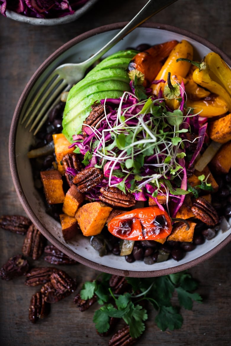 spicy Mexican Oaxacan bowl with seasoned black beans, roasted sweet potatoes, onions, and peppers, cabbage slaw, sliced avocado, and microgreens.