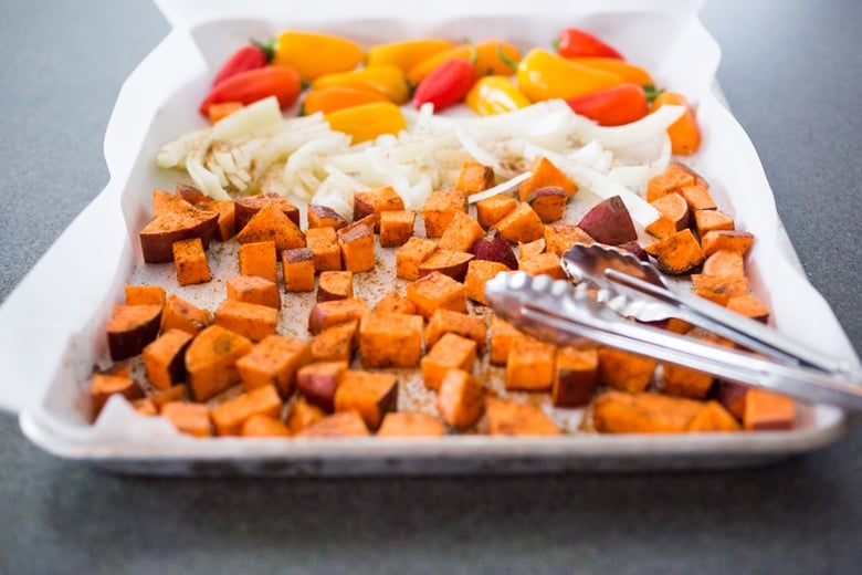 parchment lined sheet pan with sweet potatoes, sliced onions, and sweet peppers.