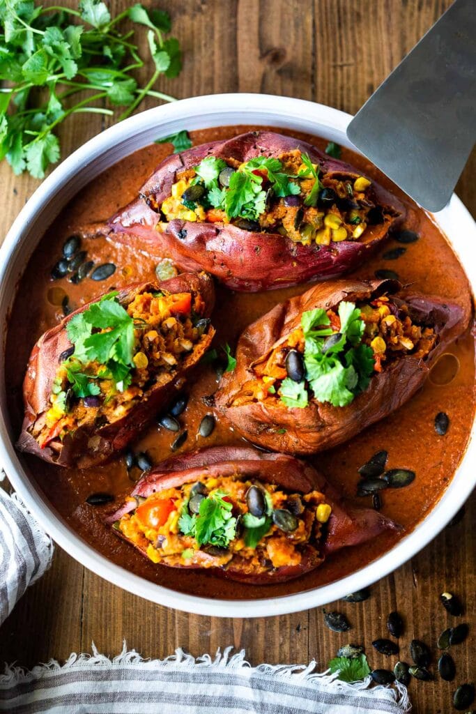 Oaxacan baked sweet potatoes stuffed with black beans, corn, peppers, and garnished with cilantro in dish with mole sauce.
