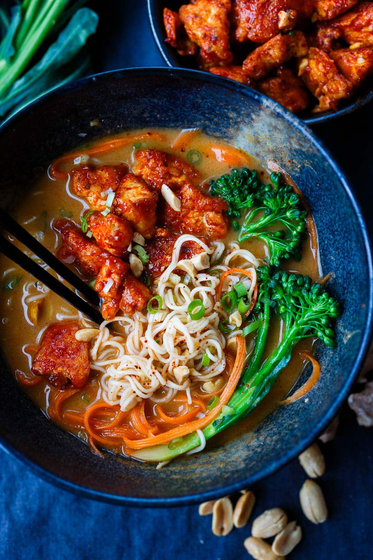 bowl of peanut butter ramen with ramen noodles, broccolini, gochujang tofu, carrots, and green onions with chopsticks. 
