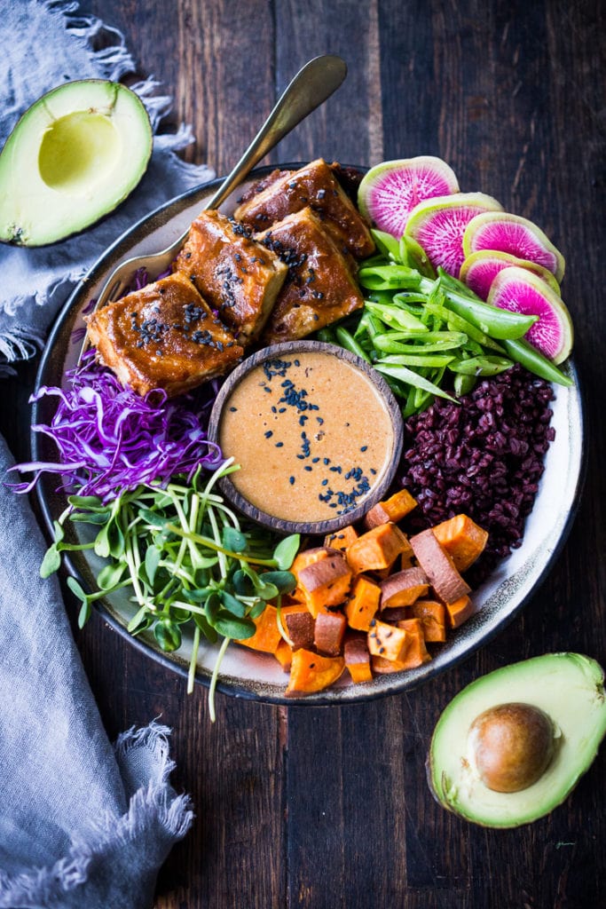 bail bowl with black rice, sweet potatoes, sprouts, cabbage, peanut tofu, snow peas, and watermelon radish, all around a small bowl of peanut sauce. 