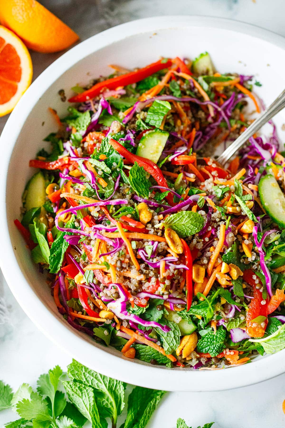 large bowl of Thai quinoa salad with crunchy cabbage, carrots, and peppers, mint, cucumber, peanuts, quinoa, with silver utensil. 