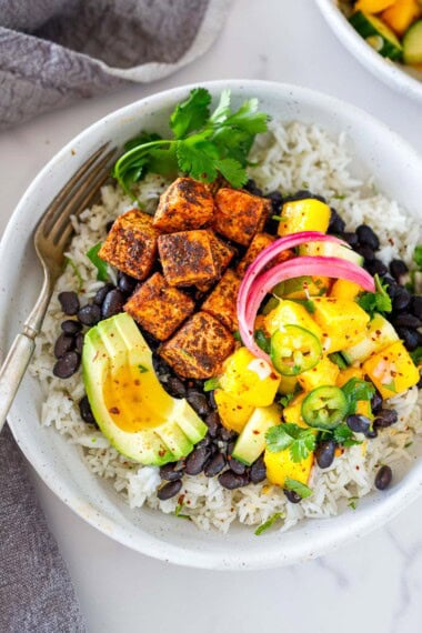 Here is one of my favorite tofu bowl recipes! Spicy jerk tofu served over black beans and rice with a refreshing mango salad, topped with pickled onions and avocado. Vegan and GF.