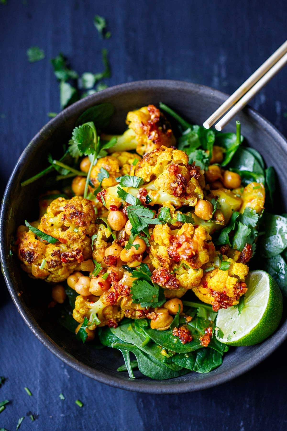 bowl of cauliflower curry vegan recipe with cilantro and chili crisp and chickpeas with lime half.