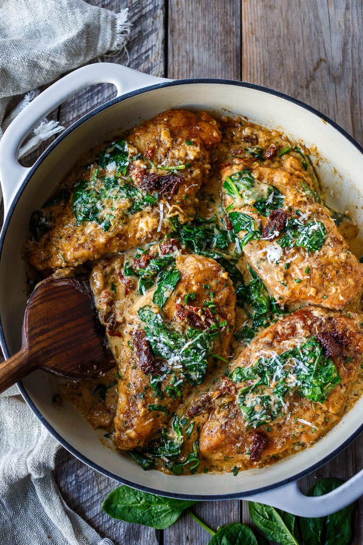 dutch oven with creamy tuscan chicken with spinach, sun-dried tomatoes-and pecorino with wood spoon. 