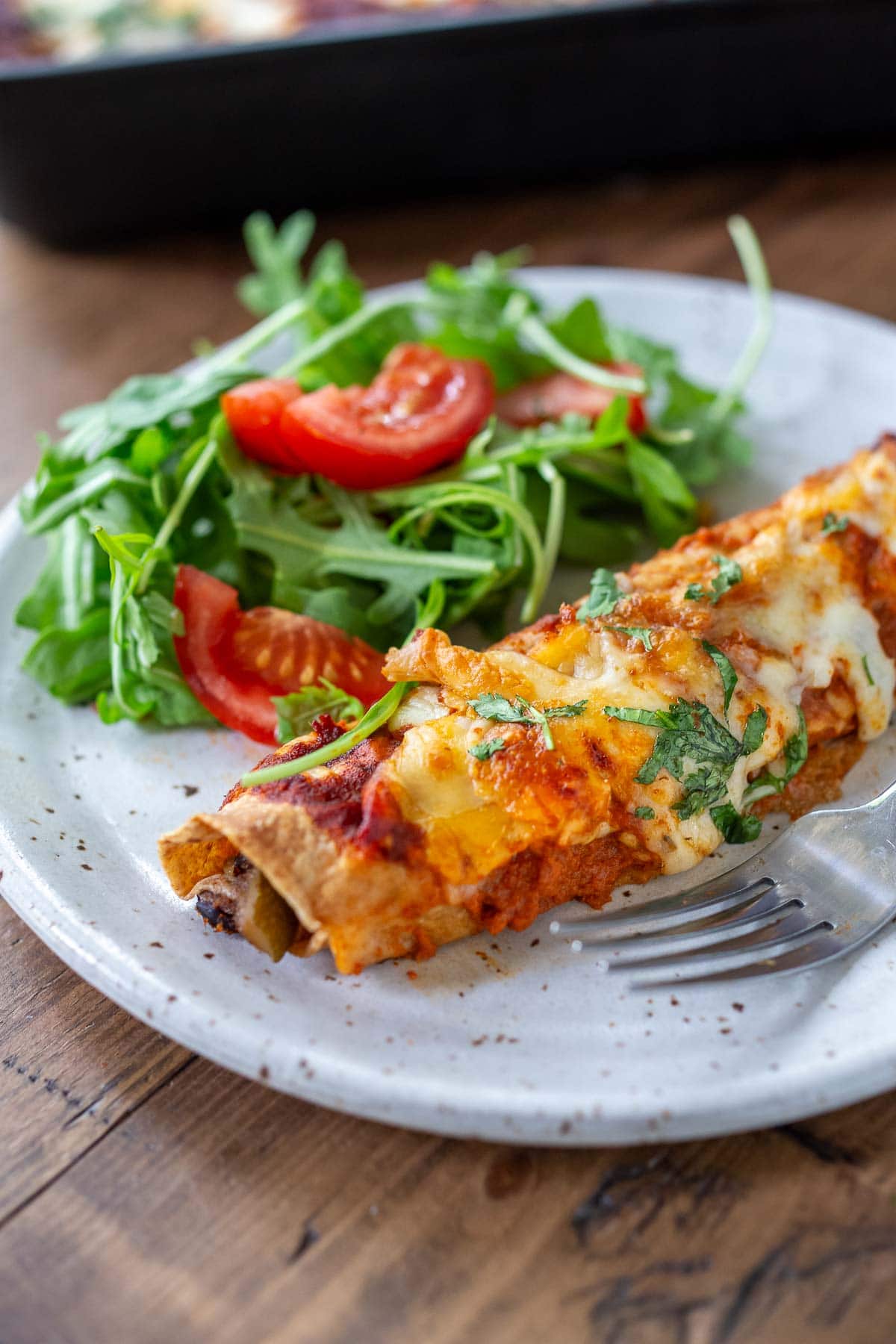 Vegetarian enchiladas on a white plate with a salad.