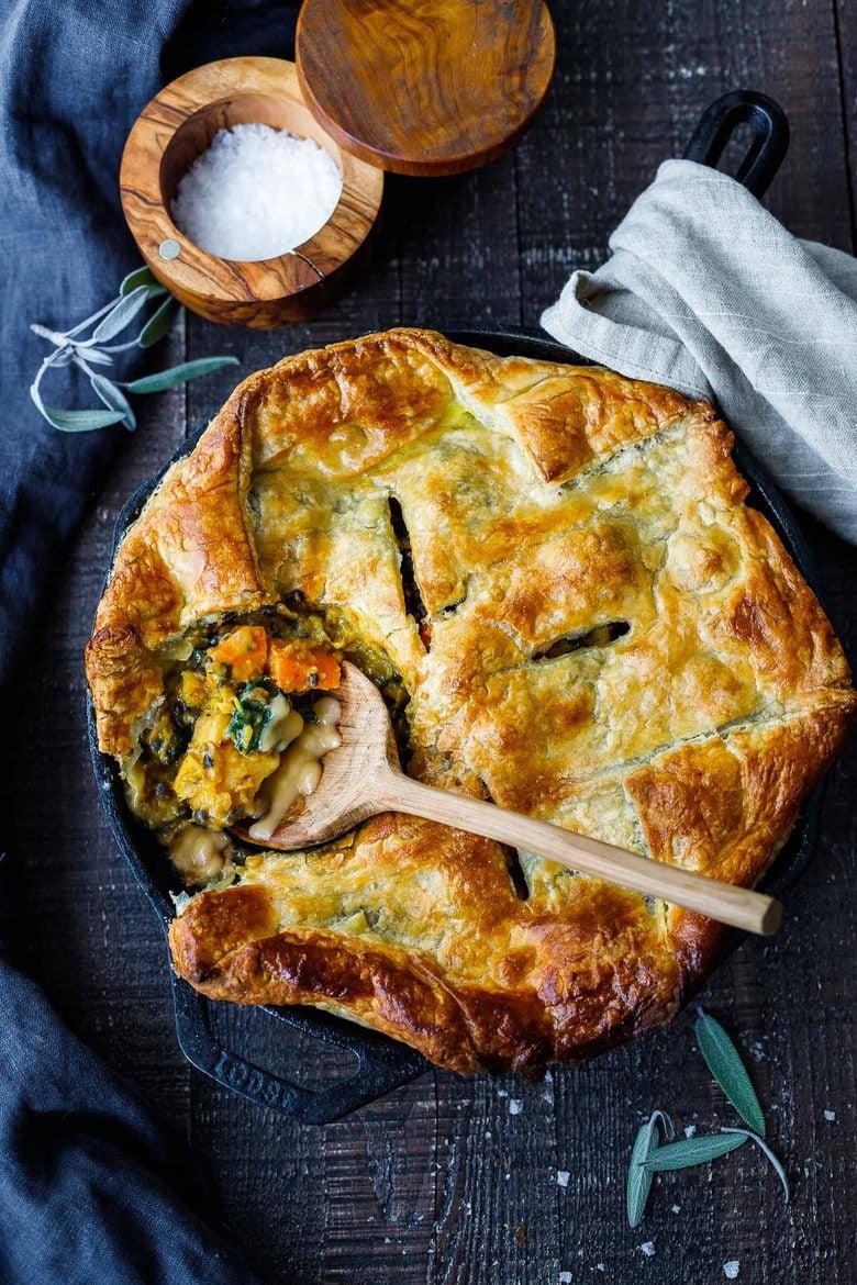 cast iron skillet with lentil pot pie with butternut squash - wood spoon gathering a spoonful from the pan. 